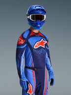 Motocross rider wearing Alpinestars 2026 Techstar Nomur Jersey, Dark Navy Orange and UCLA Blue racing gear, featuring large orange Astars logo, matching blue helmet and gloves, athletic off-road competition outfit.