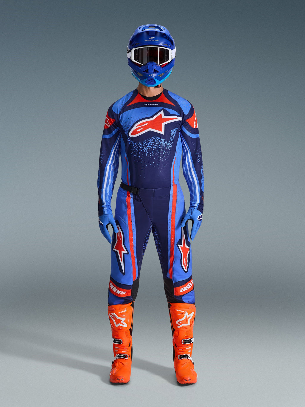 Motocross rider wearing the Alpinestars 2026 Techstar Nomur Jersey in Dark Navy, Orange, and UCLA Blue, paired with matching motocross pants, a blue helmet with goggles, and bright orange racing boots, full coordinated off-road competition gear