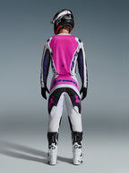 Motocross rider from behind wearing the Alpinestars 2026 Fluid Grid Gear Set, featuring a bright pink and white jersey with black sleeves, matching white pants with black and pink panels, purple Alpinestars branding, white and black racing boots, and a coordinated helmet, designed for off-road performance.