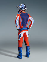 Motocross rider from the back wearing the 2026 Fluid Grid Jersey and Pants in Orange and UCLA Blue, featuring white sleeves with blue Alpinestars branding, bright blue motocross boots, and a matching helmet, complete gear set for off-road racing.