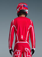 Rear view of a motocross rider wearing the Alpinestars 2026 Fluid Apex Jersey in Red and White, featuring geometric white patterns, styled with matching motocross pants and a red helmet, complete racing gear for off-road performance.