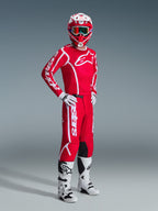 Motocross rider wearing complete Alpinestars racing gear, featuring the 2026 Fluid Apex Jersey in Red and White, matching red pants with white branding, red and white helmet with goggles, white and black motocross boots, and white gloves, professional studio shot of off-road gear.