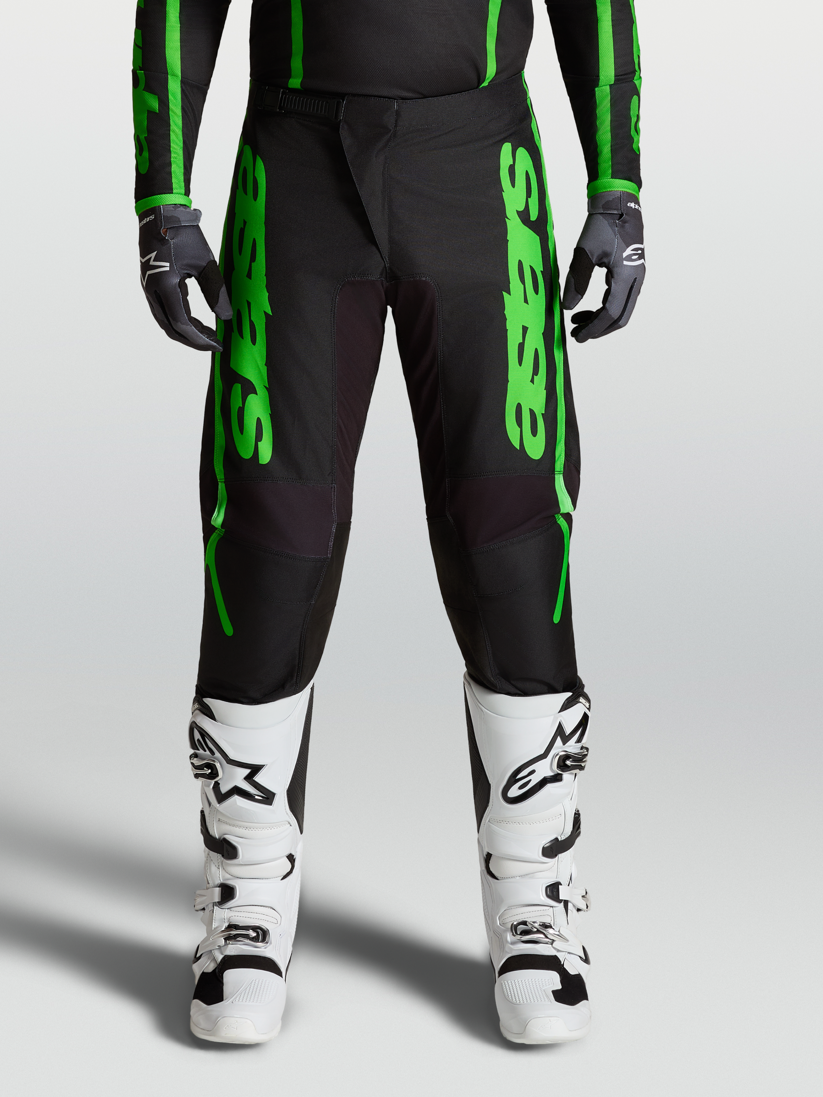 Alpinestars 2027 Fluid Apex V2 Pants, men's motocross gear in green and black, with reinforced knees and white boots.