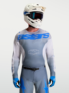 Alpinestars Racer Amber Jersey, Men's Motocross Gear in Gray and UCLA Blue, paired with a white MX helmet and goggles.