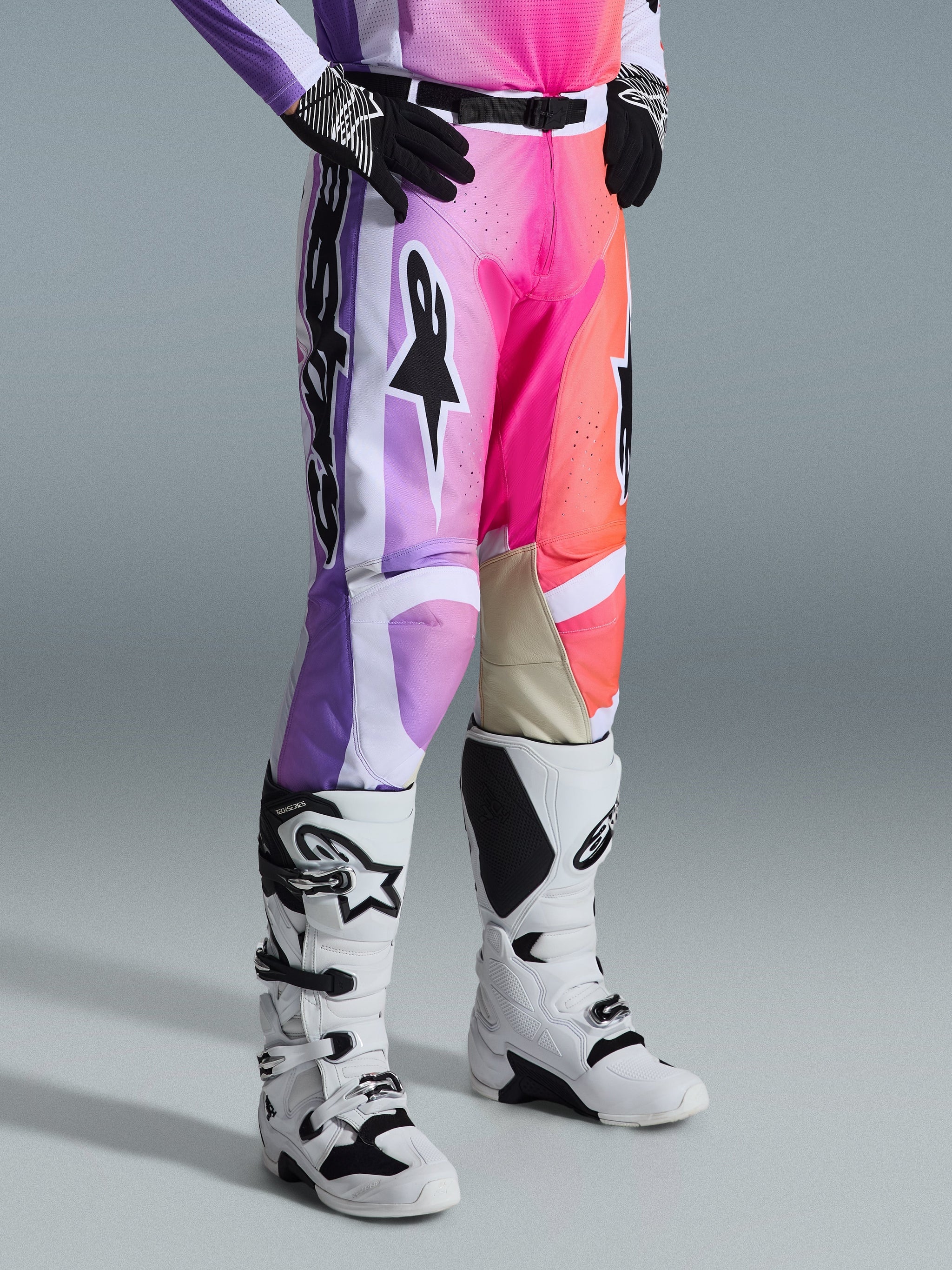 Alpinestars 2026 Racer Air Portl Pants, Motocross Pants, Multicolor graphic with purple, pink, and orange gradients, worn with white and black motocross boots and black gloves, featuring a race fit design and tan leather inner knee panels.