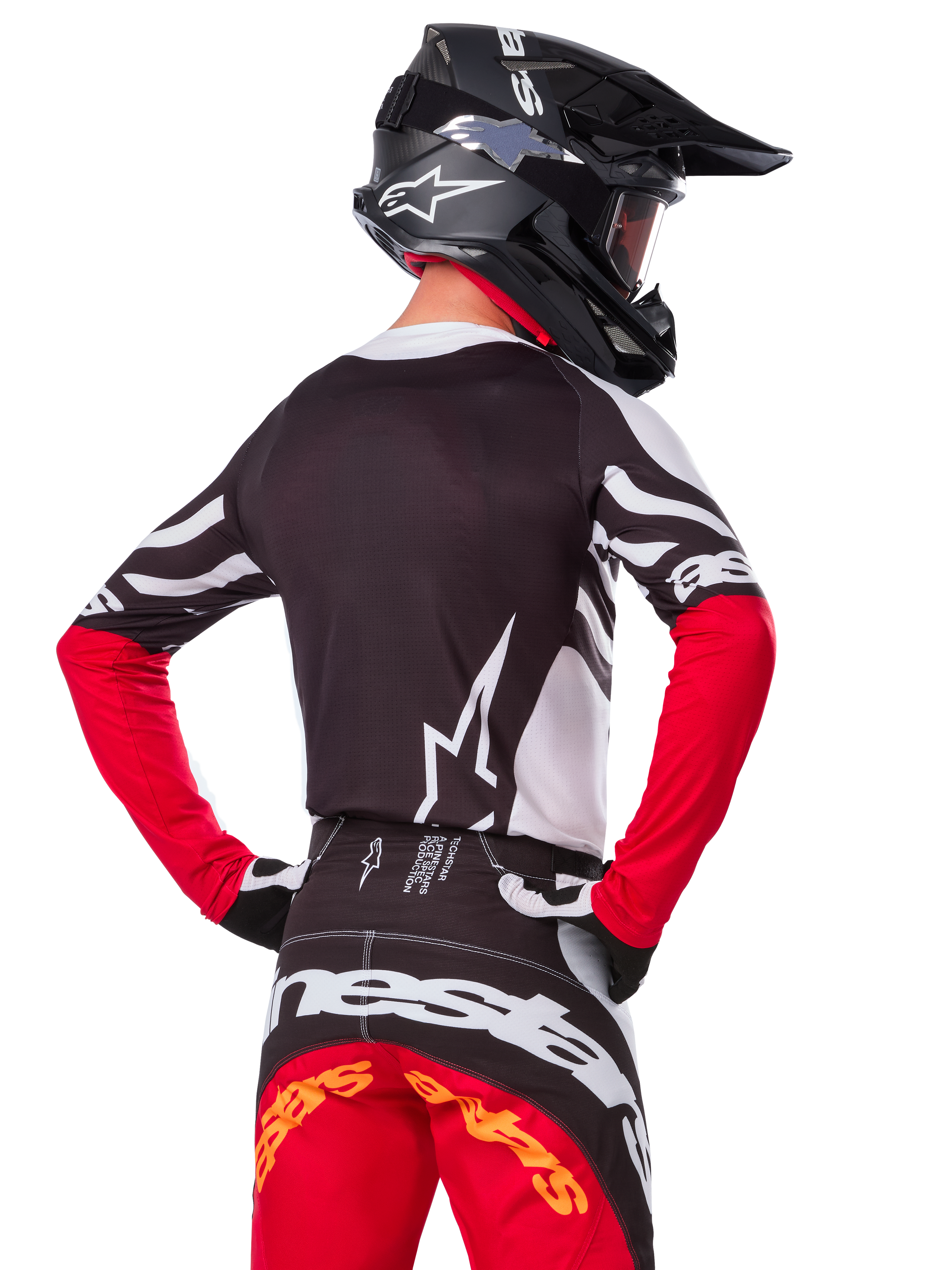 Motocross rider wearing complete racing gear, Alpinestars Limited Edition Techstar Deep Jersey in Black White and High Red, back view, matching Techstar Deep pants, black helmet with goggles, black and white gloves, professional off-road racing outfit