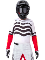 Motocross rider wearing complete racing gear, Limited Edition Techstar Deep Jersey in white and black with red sleeves, featuring wavy graphics and bold Alpinestars branding, white motocross pants, black helmet and goggles, coordinated outfit for off-road racing