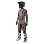 Motocross rider wearing complete racing gear featuring the Alpinestars 2024 Fluid Lurv Jersey in Mud Black, paired with matching pants, black helmet with goggles, white and black boots, and black gloves, coordinated outfit for off-road racing