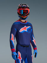 Motocross rider wearing 2026 Supertech Vista Jersey in Dark Navy, Hot Coral, and Cobalt, matching pants and gloves, multi-colored helmet with red goggles, professional gear set for off-road racing