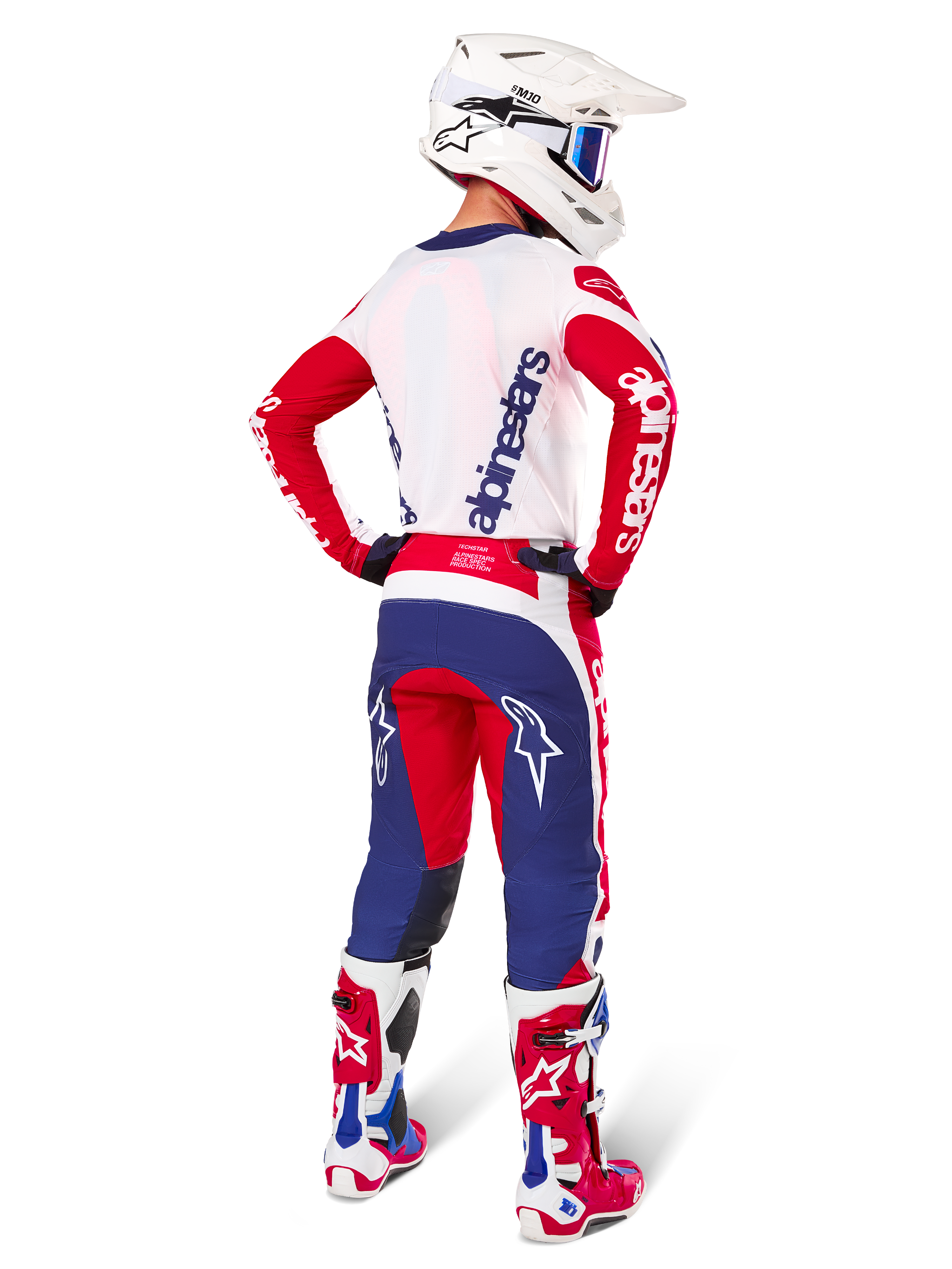 Motocross rider seen from behind wearing the Alpinestars Limited Edition Techstar Fortitude Jersey, Bright Red White and Blue color scheme, matching technical pants with star logos, white helmet with goggles, and red and white boots, complete coordinated gear for off-road racing
