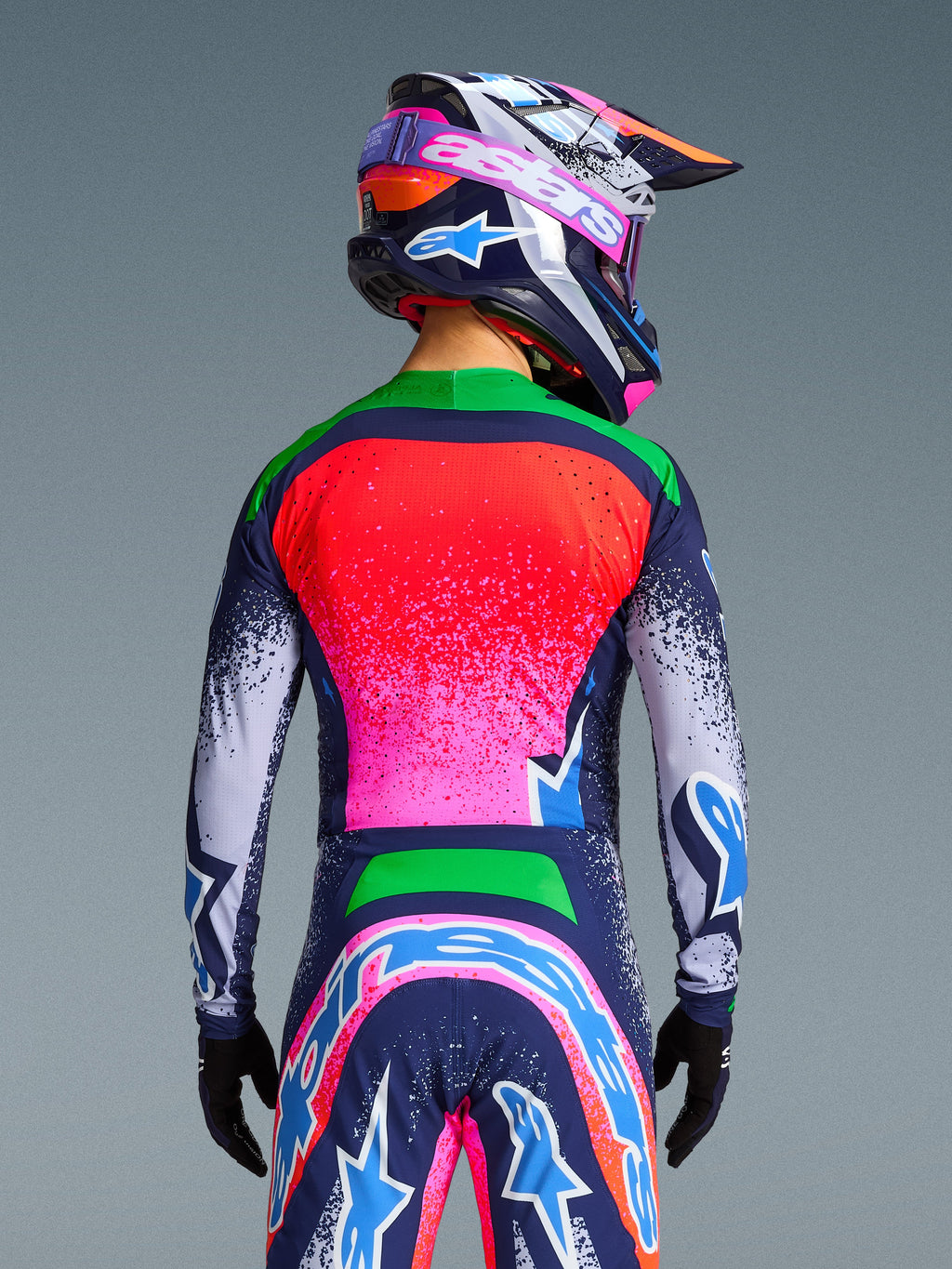 Alpinestars Limited Edition Supertech Records Jersey, rear view of a motocross rider wearing a vibrant multicolor kit, featuring a pink and red gradient back with green shoulders and navy blue speckled sleeves, styled with a matching helmet and pants for a professional off-road racing look.