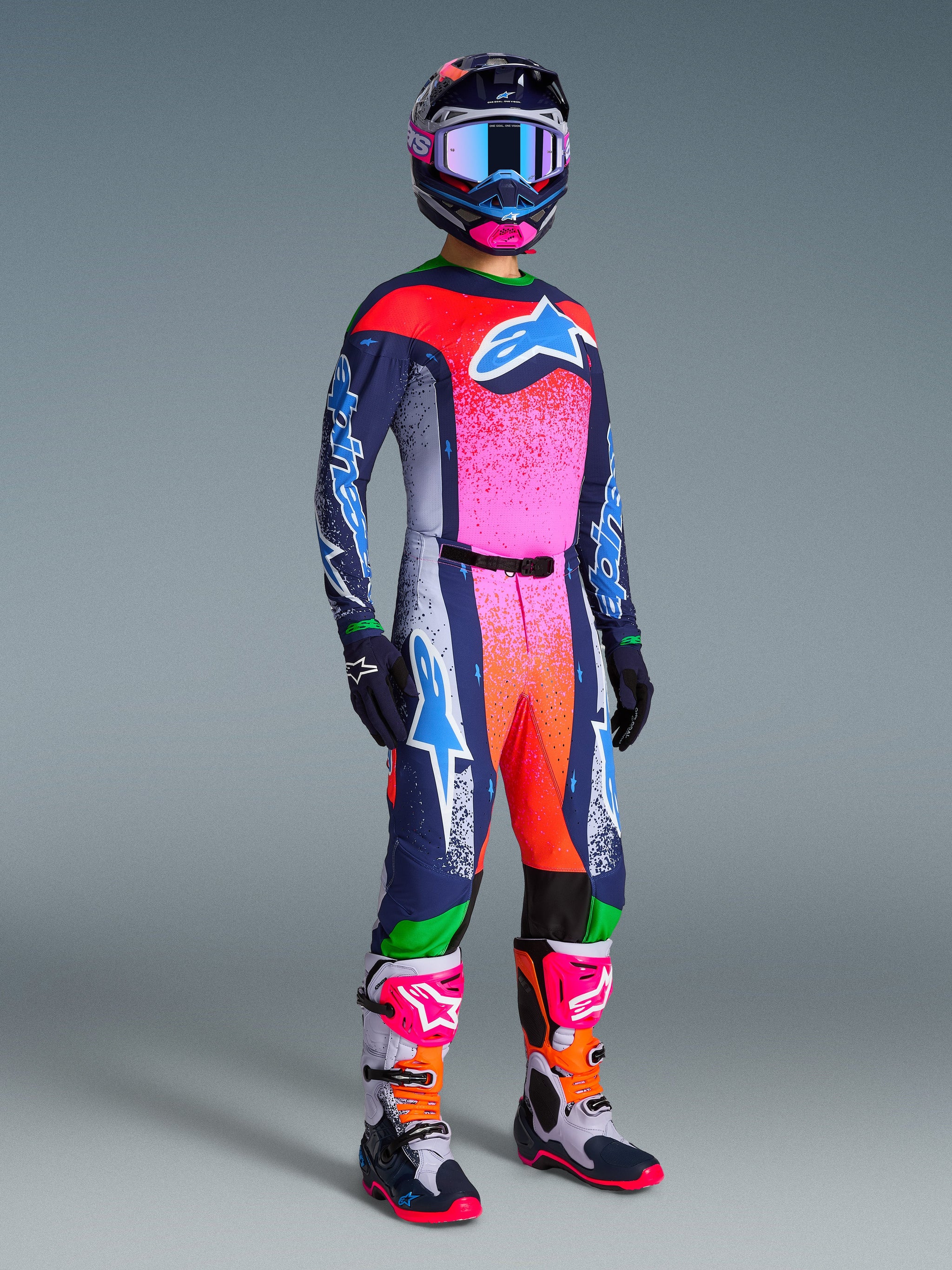 Motocross rider wearing the Alpinestars Limited Edition Supertech Records Gear Set, featuring a vibrant pink, orange, and navy blue gradient jersey and pants, matching patterned helmet and goggles, navy gloves, and coordinated racing boots, complete professional off-road racing outfit