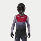 Motocross rider wearing the Alpinestars 2024 Supertech Dade Jersey in Iron Red Berry, featuring a red chest panel and gray sleeves with silver branding, worn with matching pants, a black helmet, and black gloves, professional off-road racing gear