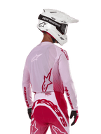 Motocross rider viewed from the back wearing the Alpinestars 2024 Supertech Dade Jersey in Red Berry Lilac, featuring breathable mesh panels and red Alpinestars logos, paired with matching red and lilac pants and a white Alpinestars helmet with goggles, professional off-road racing gear