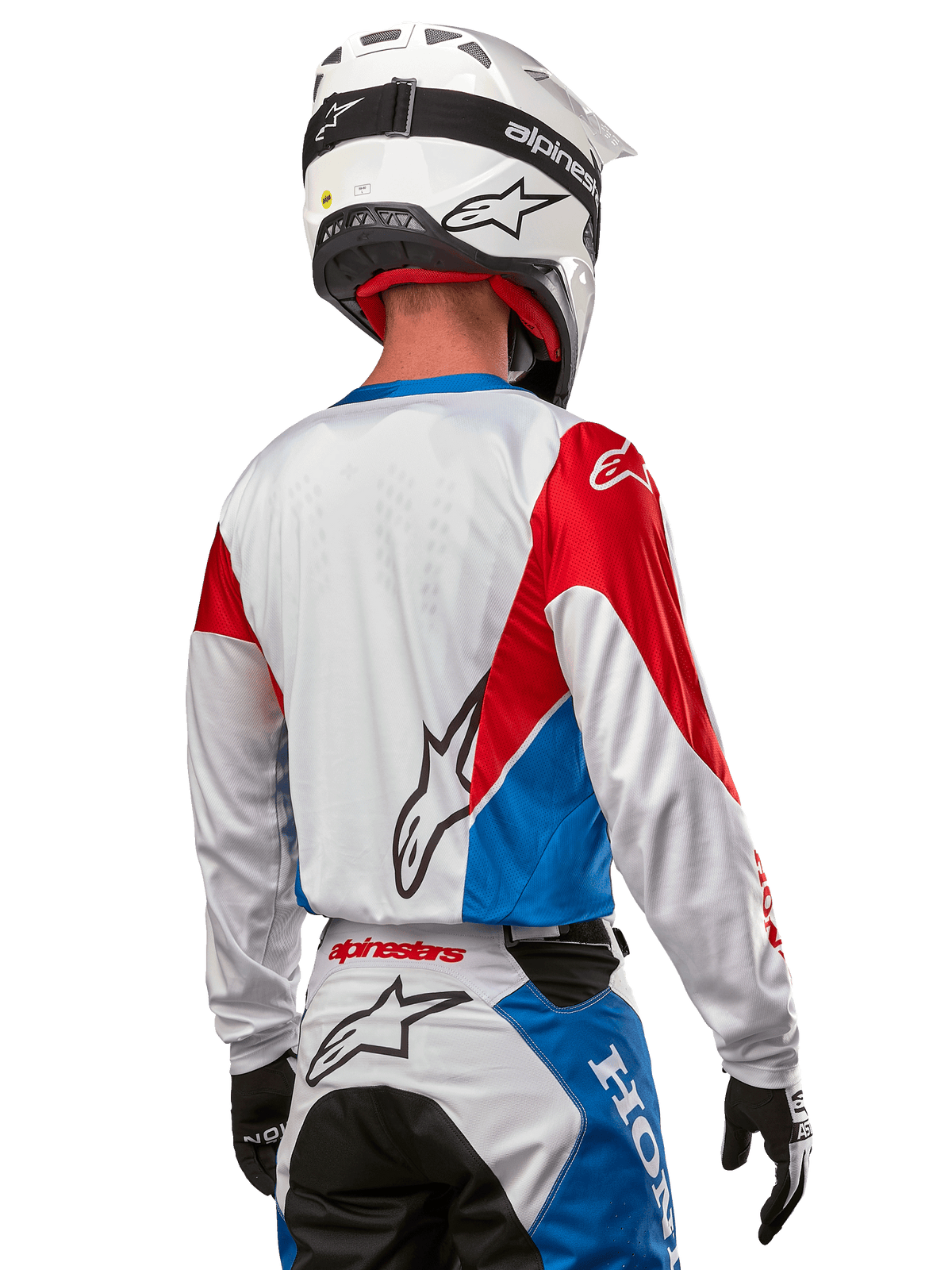 Motocross rider wearing the Alpinestars Honda Racer Iconic Jersey, back view, White with Bright Blue and Bright Red panels, featuring prominent Alpinestars logo on the back, paired with a white motocross helmet and matching racing pants.