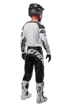 Alpinestars 2024 Racer Hana Jersey, back view of motocross rider, White and Black, white jersey with black graphic branding on sleeves, paired with black pants featuring white Alpinestars lettering on the seat, black helmet, and white and black boots, coordinated off-road racing gear