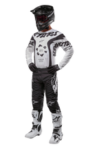 Motocross rider wearing full gear featuring the Alpinestars 2024 Racer Hana Jersey in white and black, black motocross pants with white logos, black helmet, white and black racing boots, and black gloves, professional off-road racing outfit