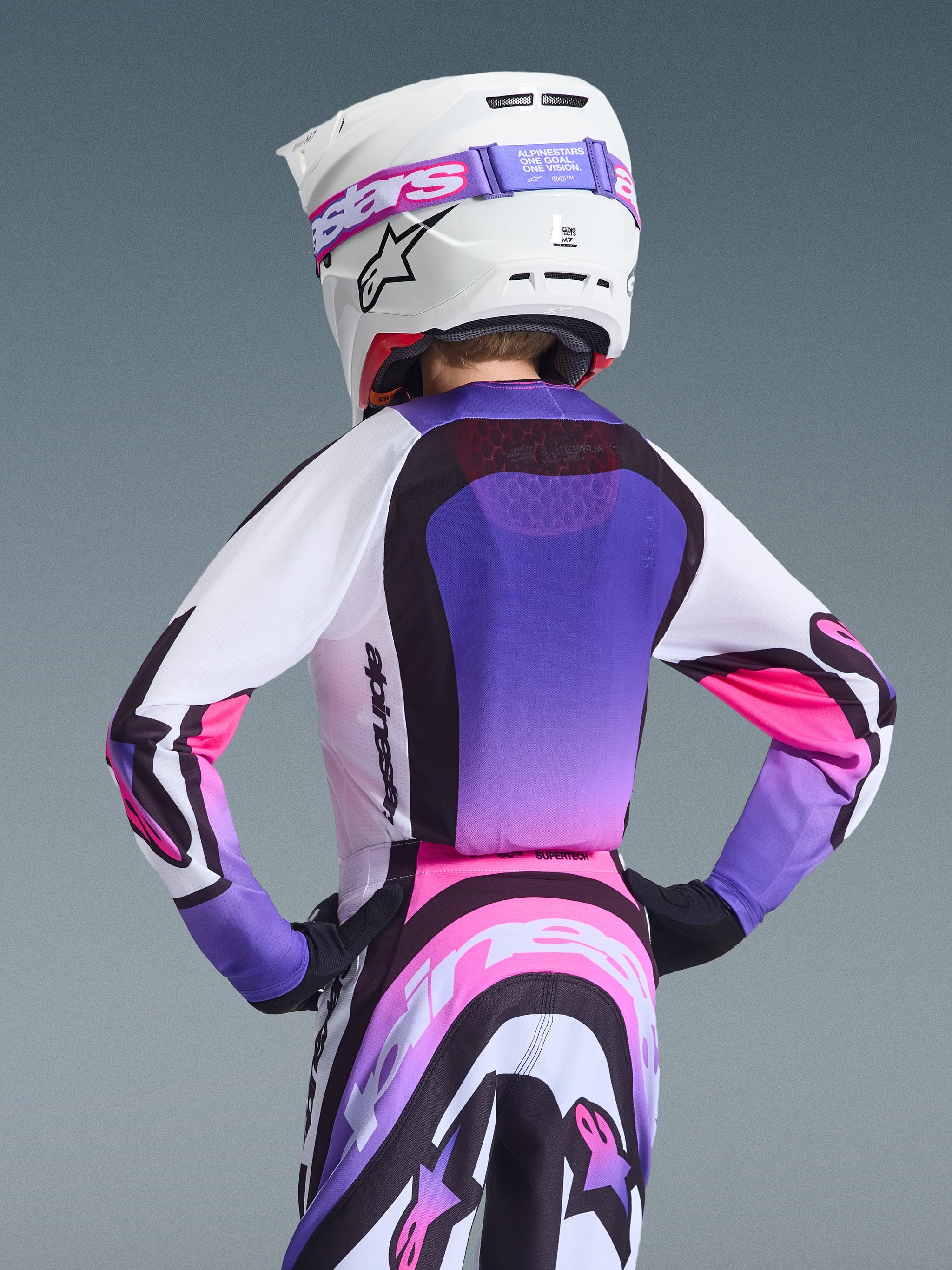 Alpinestars 2026 Youth Supertech Vista Jersey, Motocross Jersey, White Purple and Black with pink gradient accents, rear view on a youth rider wearing matching pants and a white helmet, athletic racing fit with mesh ventilation, professional motocross gear