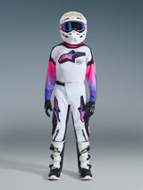 Youth motocross rider wearing complete racing gear, 2026 Youth Supertech Vista Jersey in white with pink and purple gradient sleeves, matching white and black pants with purple accents, white helmet with purple goggles, black and white boots, black gloves, coordinated high-performance outfit for off-road racing