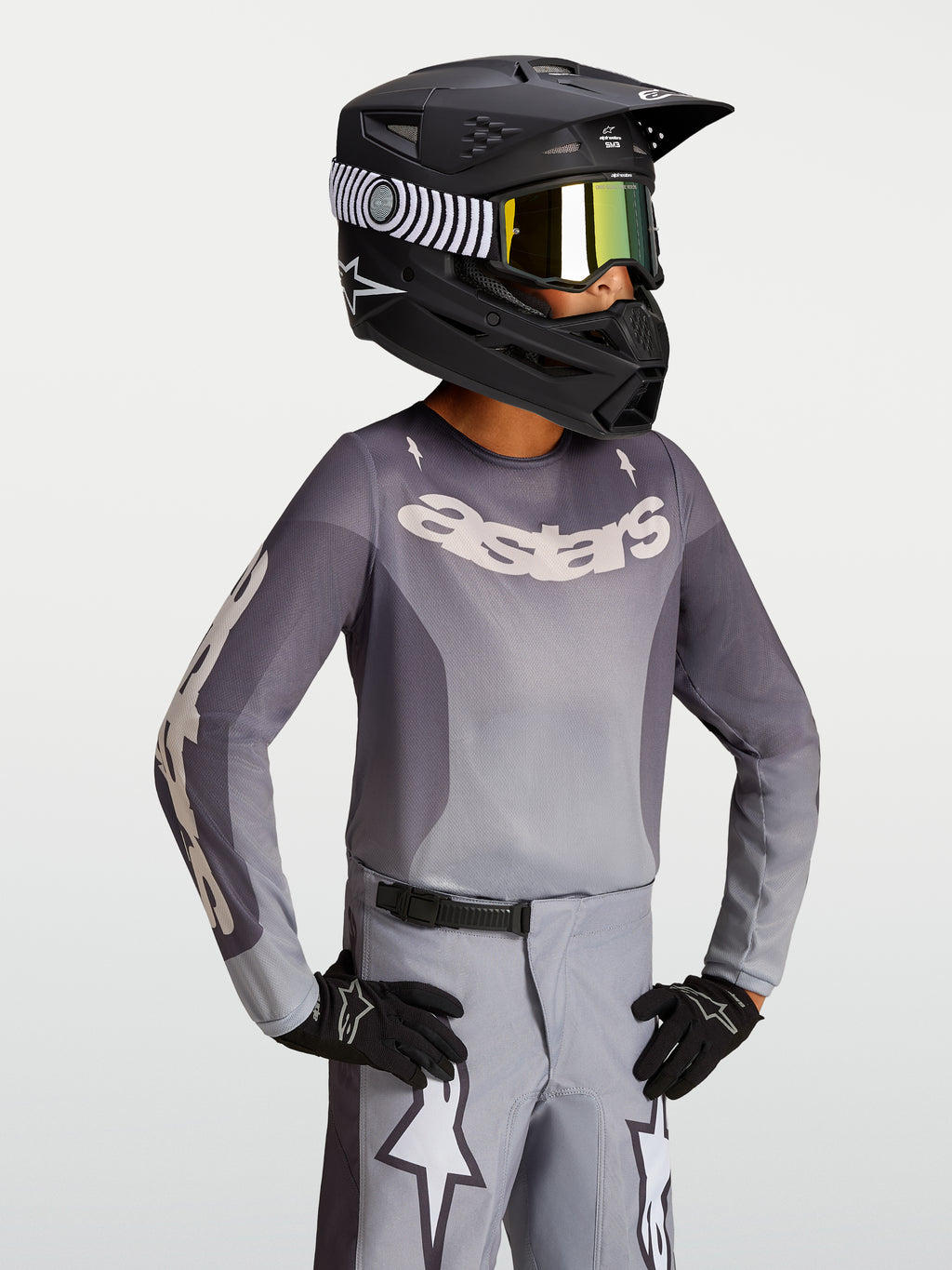 Alpinestars 2027 Youth Fluid Amber Jersey, youth motocross jersey in sand and gray, on-model with a black racing helmet.