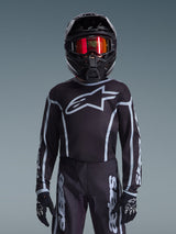 Youth motocross rider wearing Alpinestars 2026 Youth Fluid Apex Jersey in Black and Gray, matching pants, black helmet with red reflective goggles, and black gloves, coordinated off-road racing gear.