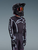 Alpinestars 2026 Youth Fluid Apex Jersey in Black and Gray, worn by a young rider with a matching black helmet and tinted goggles, featuring prominent Alpinestars branding on the chest and sleeves, part of a coordinated motocross gear set.