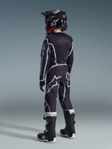 Alpinestars 2026 Youth Fluid Apex Jersey, Motocross Jersey, Black and Gray, worn with matching Youth Fluid Grid Pants, black helmet, and black and white boots, back view showing full off-road racing gear for young riders