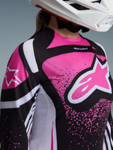 Close-up of a female rider wearing the Alpinestars 2026 Stella Techstar Nomur Jersey in Black White and Fuchsia, featuring a bold pink star logo on the chest and a white motocross helmet.