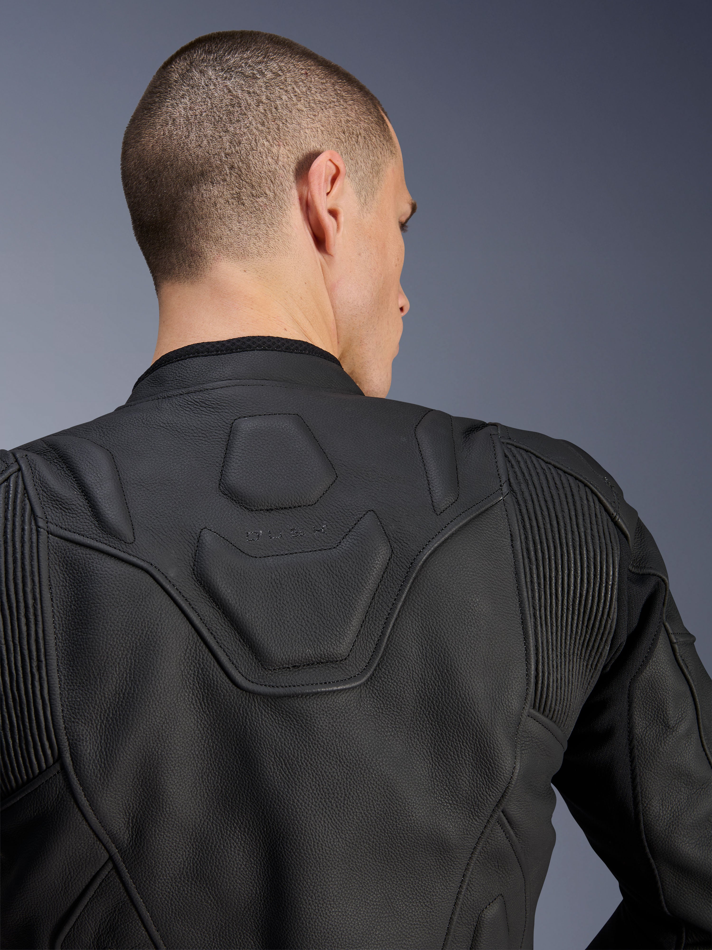 Alpinestars Dusk Leather Jacket, Black, close-up of the upper back and shoulders showing the embossed DUSK logo on a padded panel, leather accordion stretch inserts, premium bovine leather construction