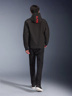 Alpinestars Radium Tech Hoodie, urban motorcycle jacket, Black, back view featuring bright red 'ALPINE' text on the hood, worn with black pants and sneakers, sleek technical shell for commuting.