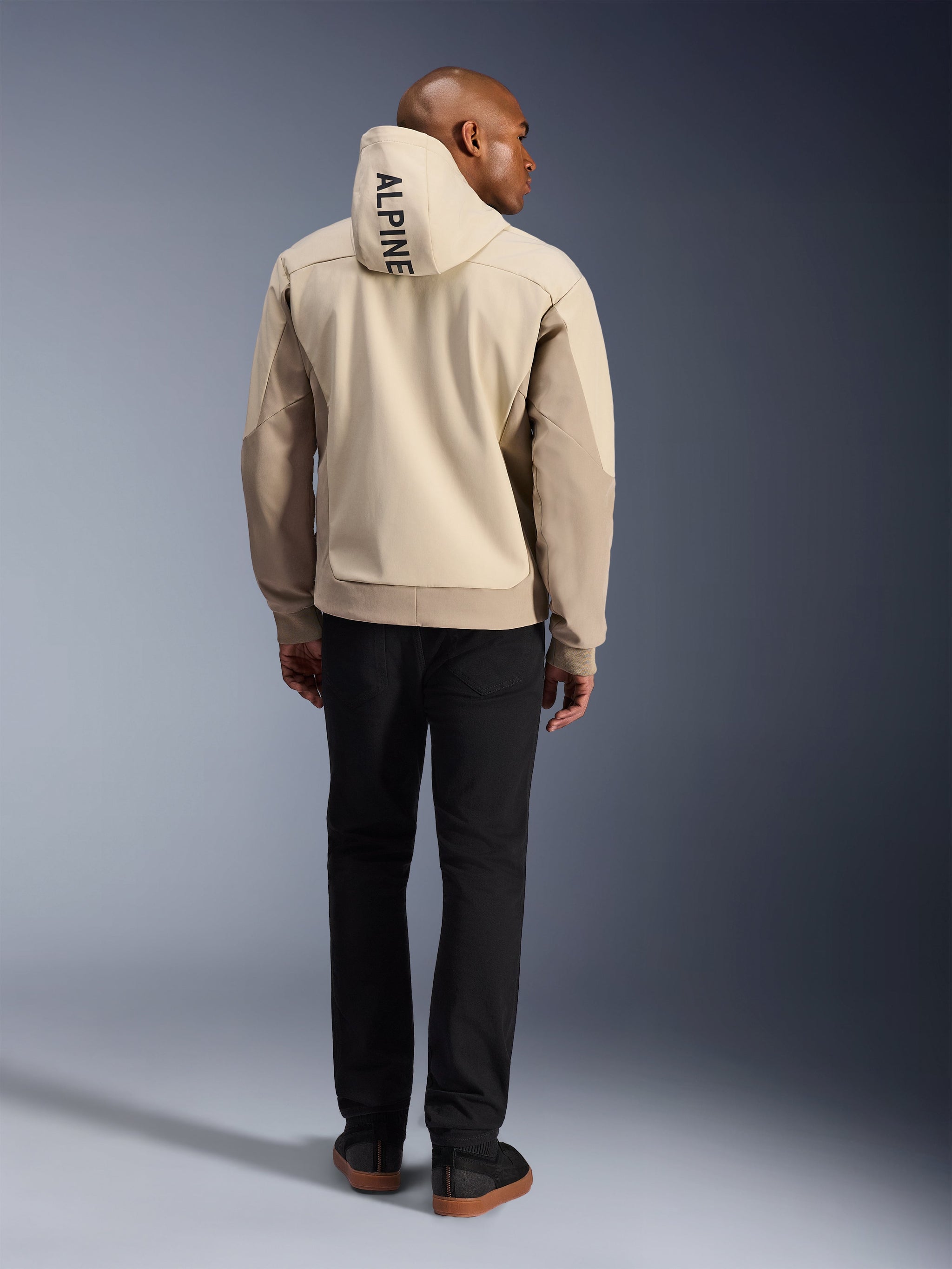 Alpinestars Radium Tech Hoodie, Mastic Aluminum, back view showing vertical 'ALPINE' text on the hood, technical 3L windproof shell urban motorcycle jacket with tan panels, worn with black pants