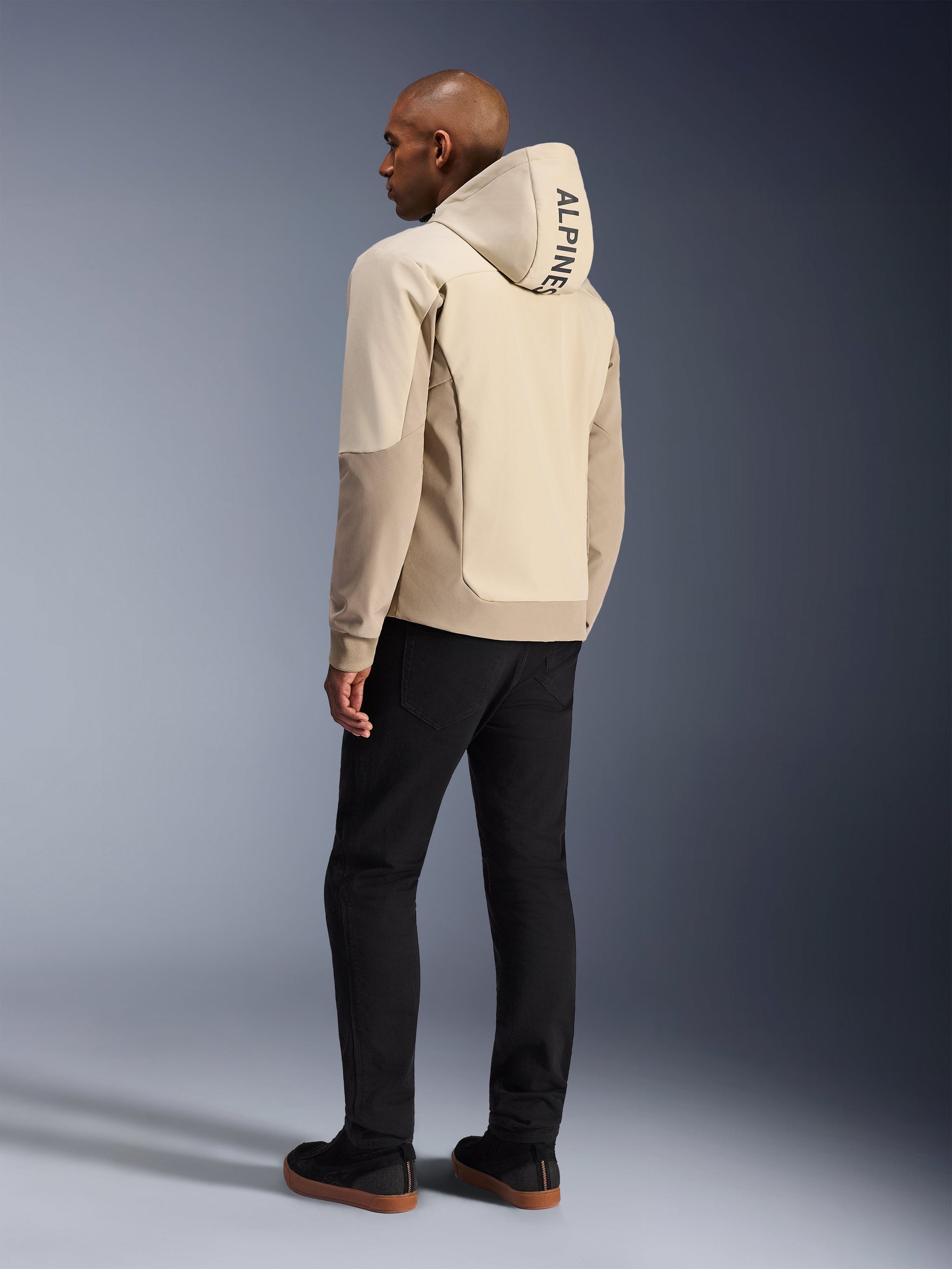 Alpinestars Radium Tech Hoodie in Mastic Aluminum, urban motorcycle jacket, rear view on model with hood up, vertical ALPINESTARS branding on hood, paired with black pants, modern textile construction for urban riding protection.