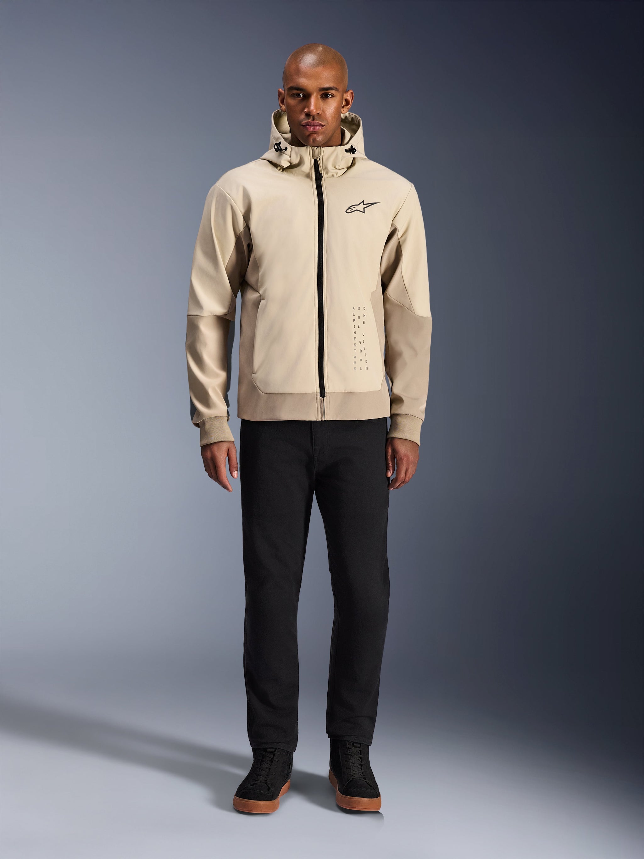 Alpinestars Radium Tech Hoodie in Mastic Aluminum, urban motorcycle hoodie worn by a male model with black pants and black boots, featuring a full-length black zipper, small chest logo, and athletic fit for city riding.