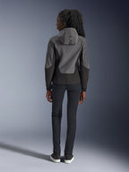 Woman wearing Alpinestars Stella Radium Tech Hoodie, Deep Gray and Black, back view showing 'ALPIN' branding on the hood, paired with slim-fit black pants and black sneakers, urban motorcycle riding apparel