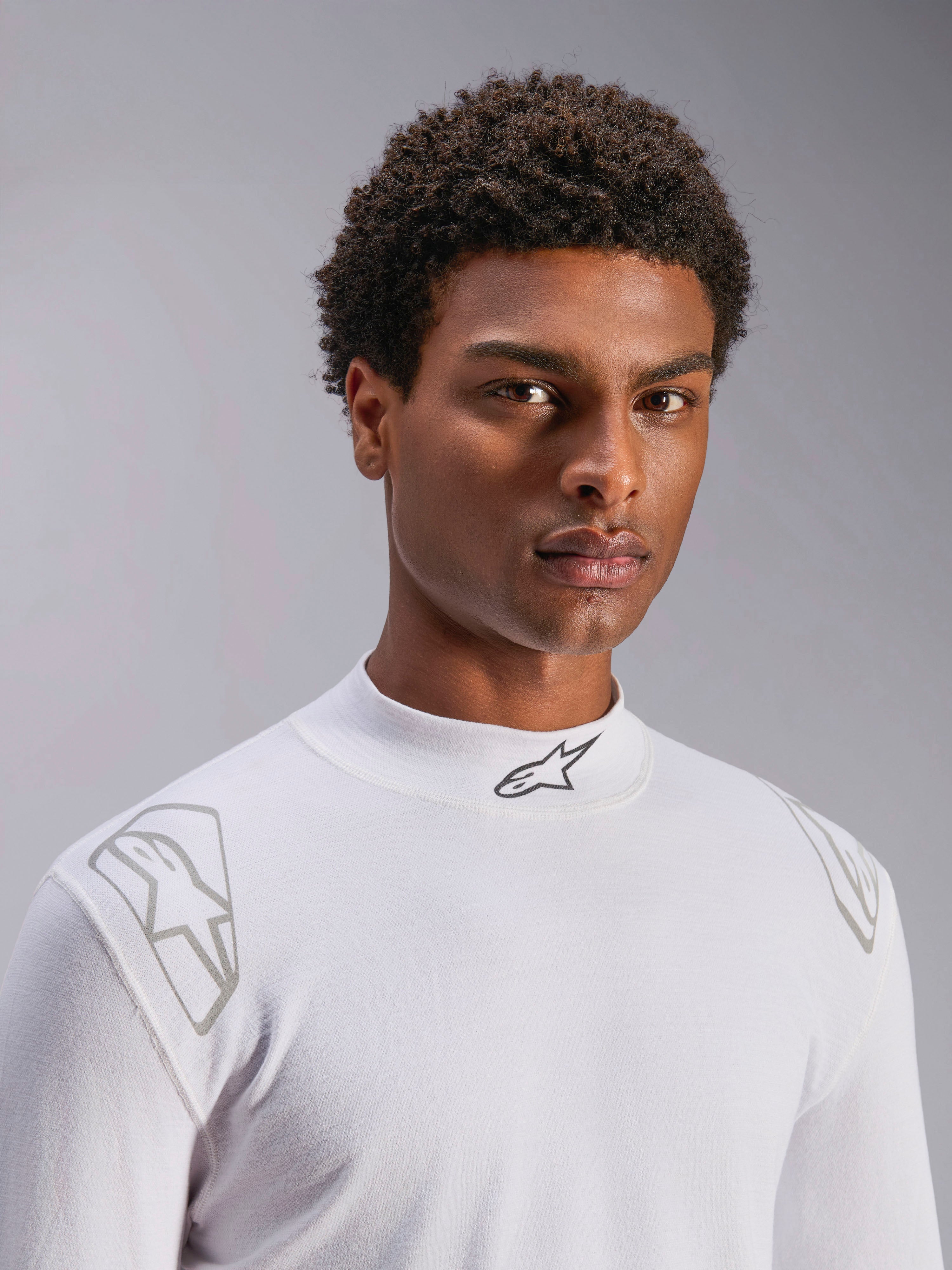 Alpinestars ZX Evo V3 Top - Long Sleeve, White Auto Racing Base Layer, worn by a male model, mock neck with black Alpinestars logo, silver graphic prints on the shoulders, lightweight flame-resistant motorsport underwear