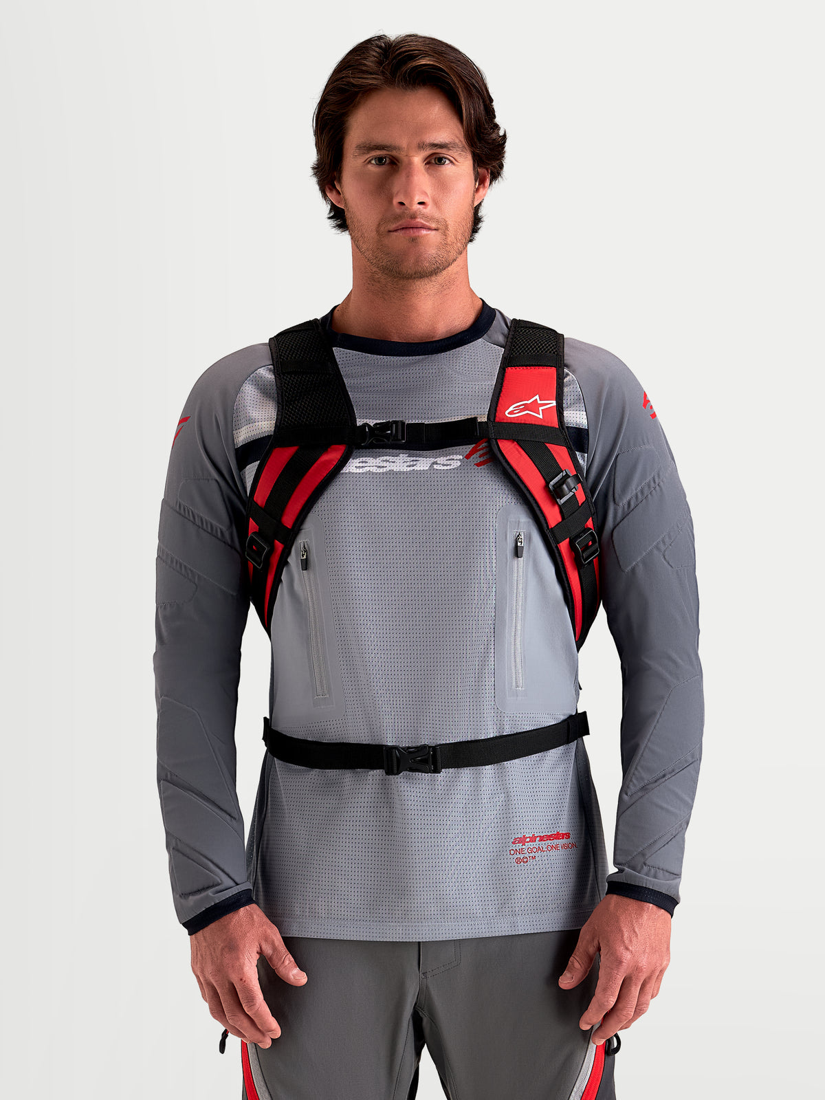 Alpinestars AT-9 Backpack, motocross backpack worn by a male model, black and bright red with padded shoulder straps and harness system, lightweight textile construction