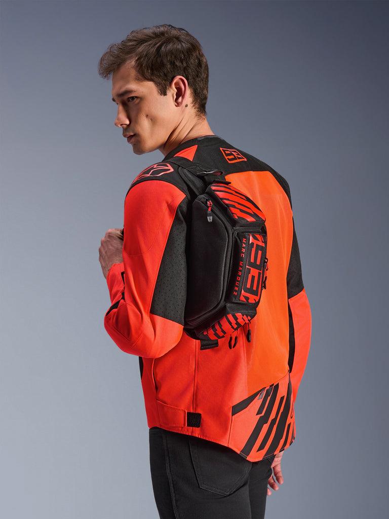 Alpinestars MM93 Waist Bag, Black with Red Fluo and Bright Red, worn by a model across the back over a red and black motorcycle jacket, featuring bold MM93 branding and Marc Marquez graphics