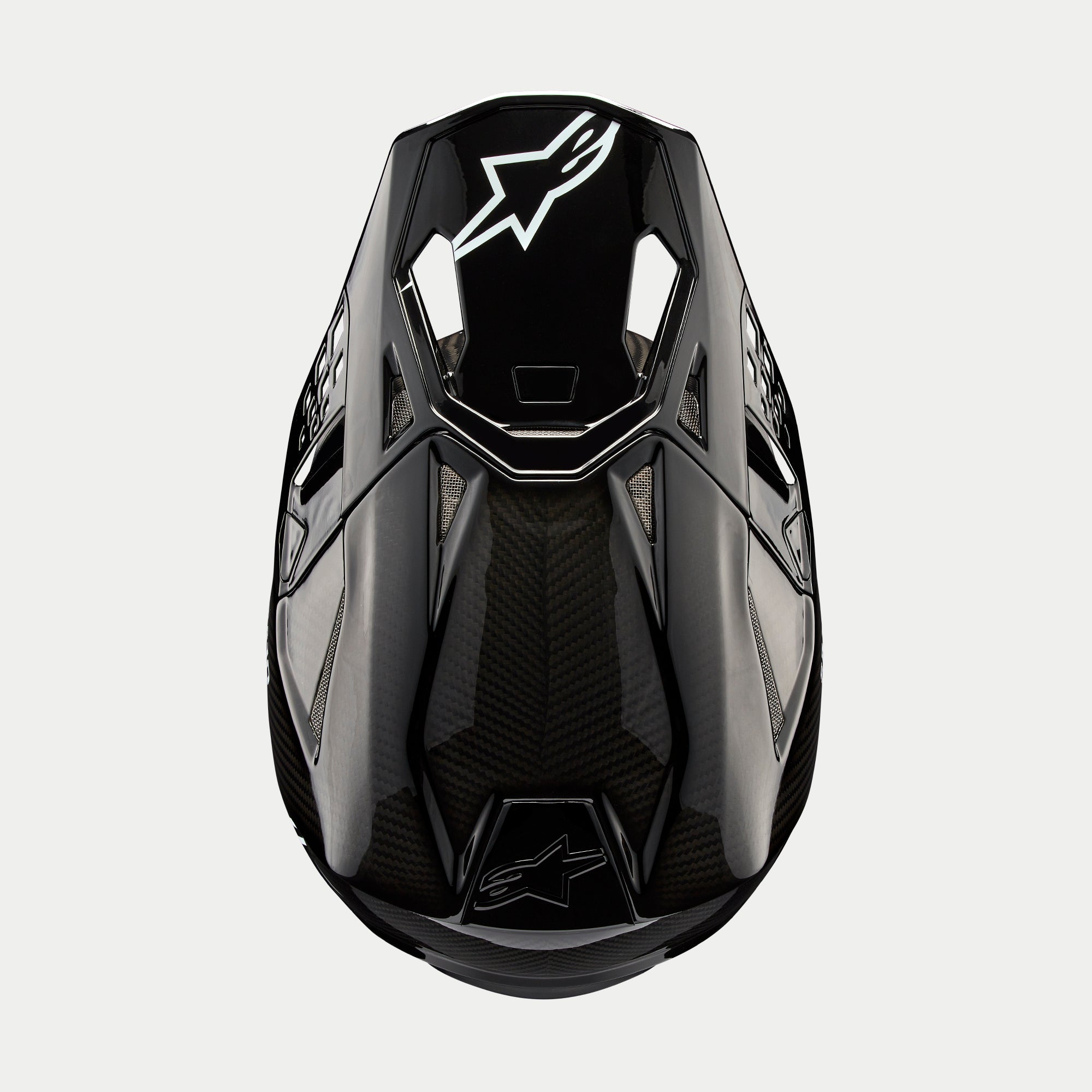 Alpinestars Supertech M10 Solid Helmet, Motocross Helmet, Black Glossy Carbon, Top-down view showing visible carbon fiber weave, white Astars logo on the visor, sleek aerodynamic profile with integrated ventilation ports