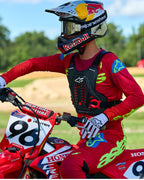Motocross rider wearing Alpinestars A-5 Plasma Chest Protector in Black and Red, paired with a red and lime green racing jersey and pants, seated on a red Honda motorcycle, high-performance off-road protective gear