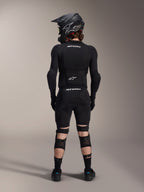 Alpinestars A-Impact Plasma Pro Knee Shin Protectors, Black, back view on a rider wearing full mountain bike protective gear including a full-face helmet and body armor, featuring a triple strap closure system and ventilated mesh panels for a secure fit and airflow