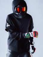 RSRV Vault Hoodie, Black Premium Streetwear Hoodie, Person wearing motorsport-inspired luxury hoodie with hood up, black helmet with reflective red-orange goggles, colorful racing gloves, sleek urban performance style