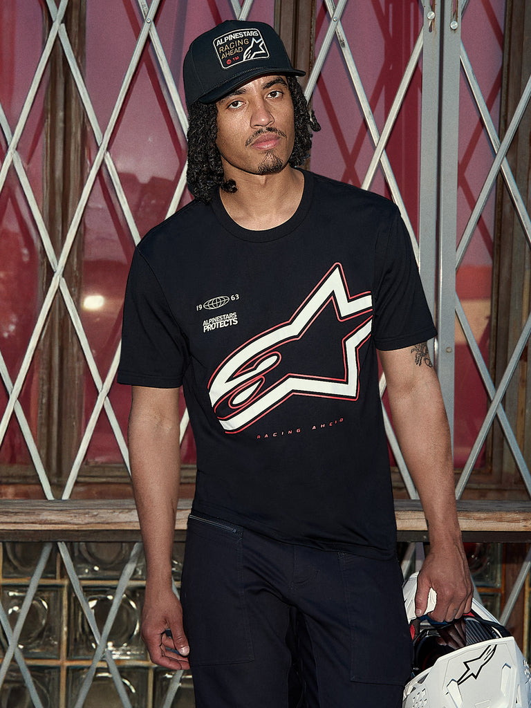 Alpinestars Authority CSF Tee, Short Sleeve T-Shirt, Black, Large white and red Astars outline logo with 'Alpinestars Protects' graphic, lifestyle shot featuring a man in a black trucker hat holding a white helmet, Casual Motorsport Streetwear