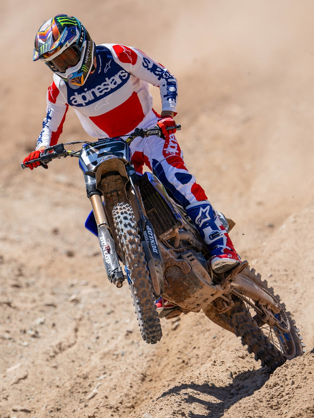 Motocross rider in action wearing Alpinestars Limited Edition Fortitude Tech 10 Boots, Bright Red White and Blue racing jersey and pants, coordinated patriotic gear set for off-road performance on a dirt track.