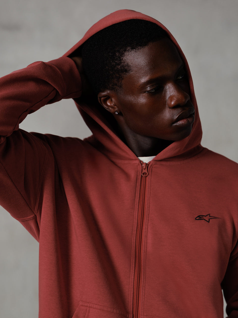 Alpinestars Essentials Ageless Zip Hoodie, Brick red, casual lifestyle streetwear, hood up with hand behind head, small black Astars logo on chest, relaxed fit fleece hoodie