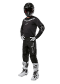 Alpinestars 2024 Fluid Graphite Gear Set, Complete Motocross Racing Outfit, Black with Gray and White Logos, featuring jersey and pants worn with matching black helmet, white and black gloves and boots, designed for off-road protection