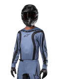 Motocross rider wearing Alpinestars 2024 Fluid Lurv Jersey, Light Blue and Black, paired with a black helmet and goggles, featuring bold black graphic accents and Alpinestars star logo, athletic performance gear for off-road racing