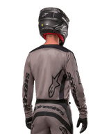 Motocross rider viewed from the back wearing the Alpinestars 2024 Fluid Lurv Jersey in Mud Black, featuring black Alpinestars branding on sleeves and back, paired with a black helmet and matching gear for off-road racing