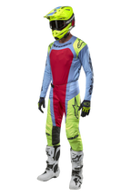 Motocross rider wearing Alpinestars 2024 Techstar Ocuri Pants in Light Blue, Yellow Fluo, and Red Berry, coordinated racing gear including matching jersey, fluo yellow helmet, and white boots, front view of off-road competition outfit.