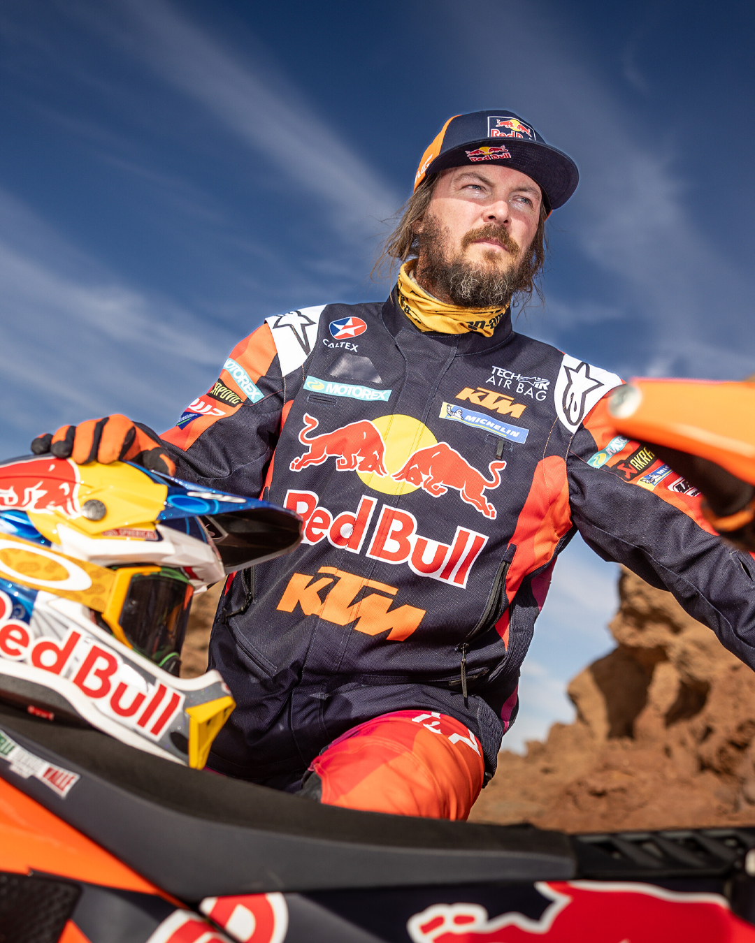 Toby Price wearing a Red Bull KTM enduro jacket by Alpinestars sitting on a motorcycle with a blue sky background