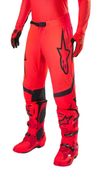 Alpinestars Supertech Ember LE Motocross Pants, Red Fluo and Bright Red with Black accents, worn with matching red racing boots and gloves, featuring a prominent black star logo on the leg, secure waist buckle, and perforated zones for ventilation.